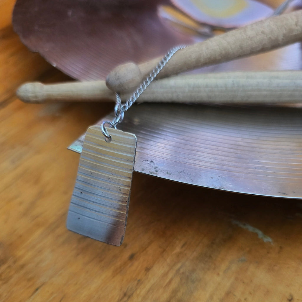 dog tag style upcycled cymbal piece necklace on drumsticks and a broken cymbal 