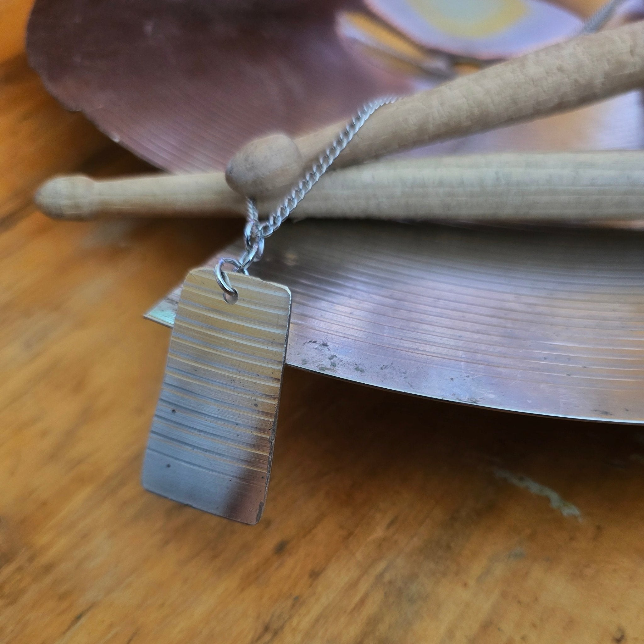 dog tag style upcycled cymbal piece necklace on drumsticks and a broken cymbal 