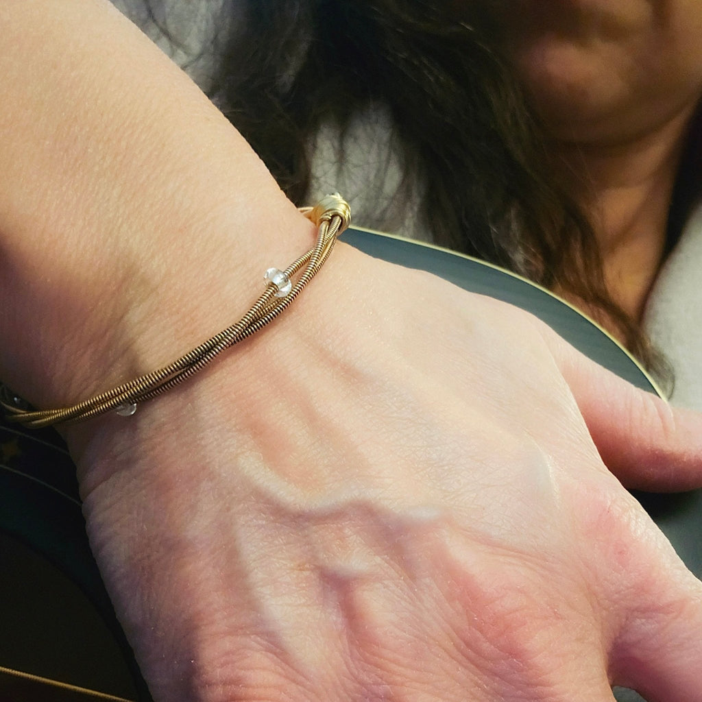 face of woman holding a black guitar on her wrist is a bronze coloured guitar string and glass bead bangle