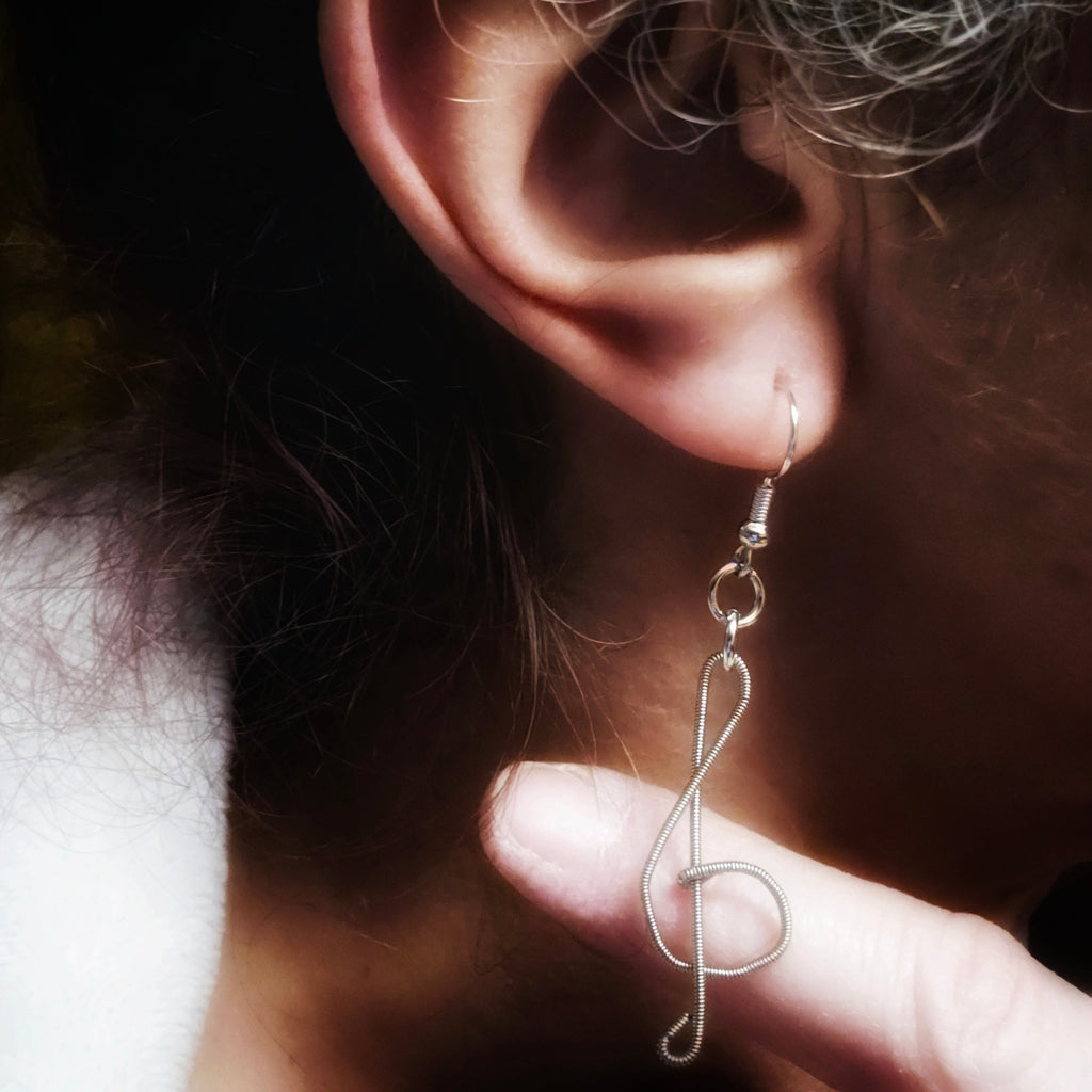 Woman's ear wearing a treble clef shaped earrings made from upcycled guitar strings 