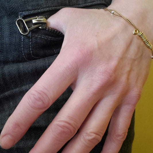 woman's hand and wrist wearing a copper coloured bangle style guitar string bracelet with clear glass beads 