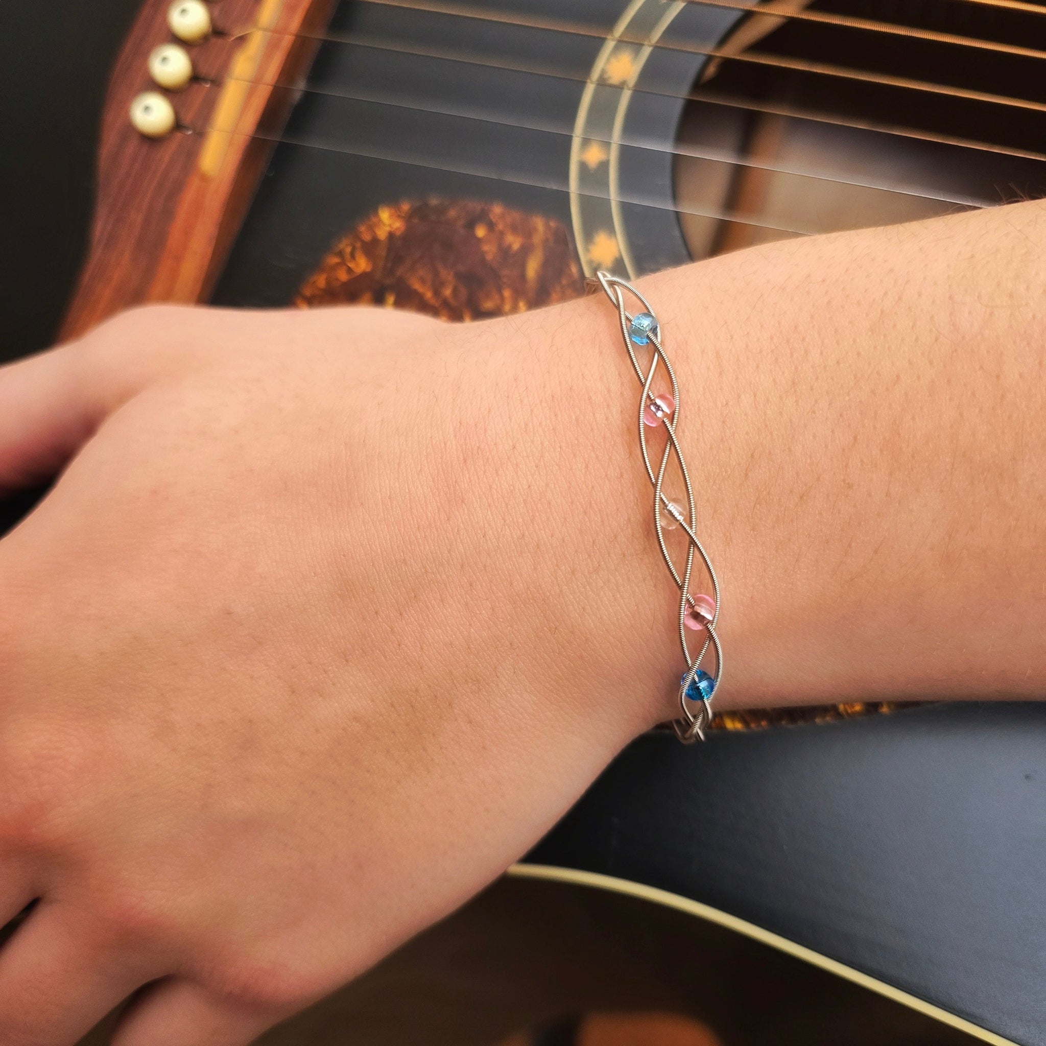 wrist wearing braided trans pride guitar string bracelet on black guitar
