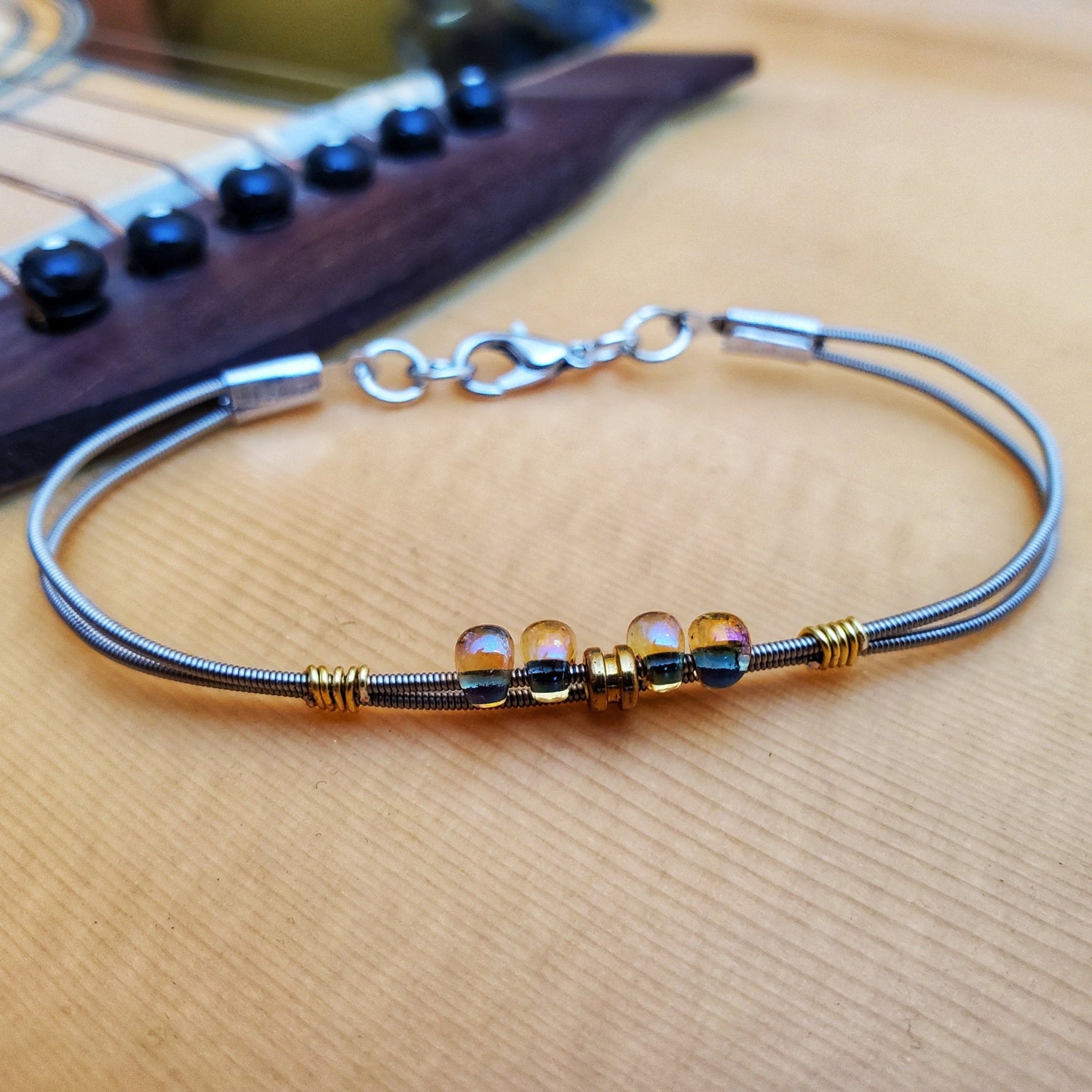 guitar string bracelet with multicoloured glass beads and a gold coloured guitar string balled sitting on an acoustic guitar body