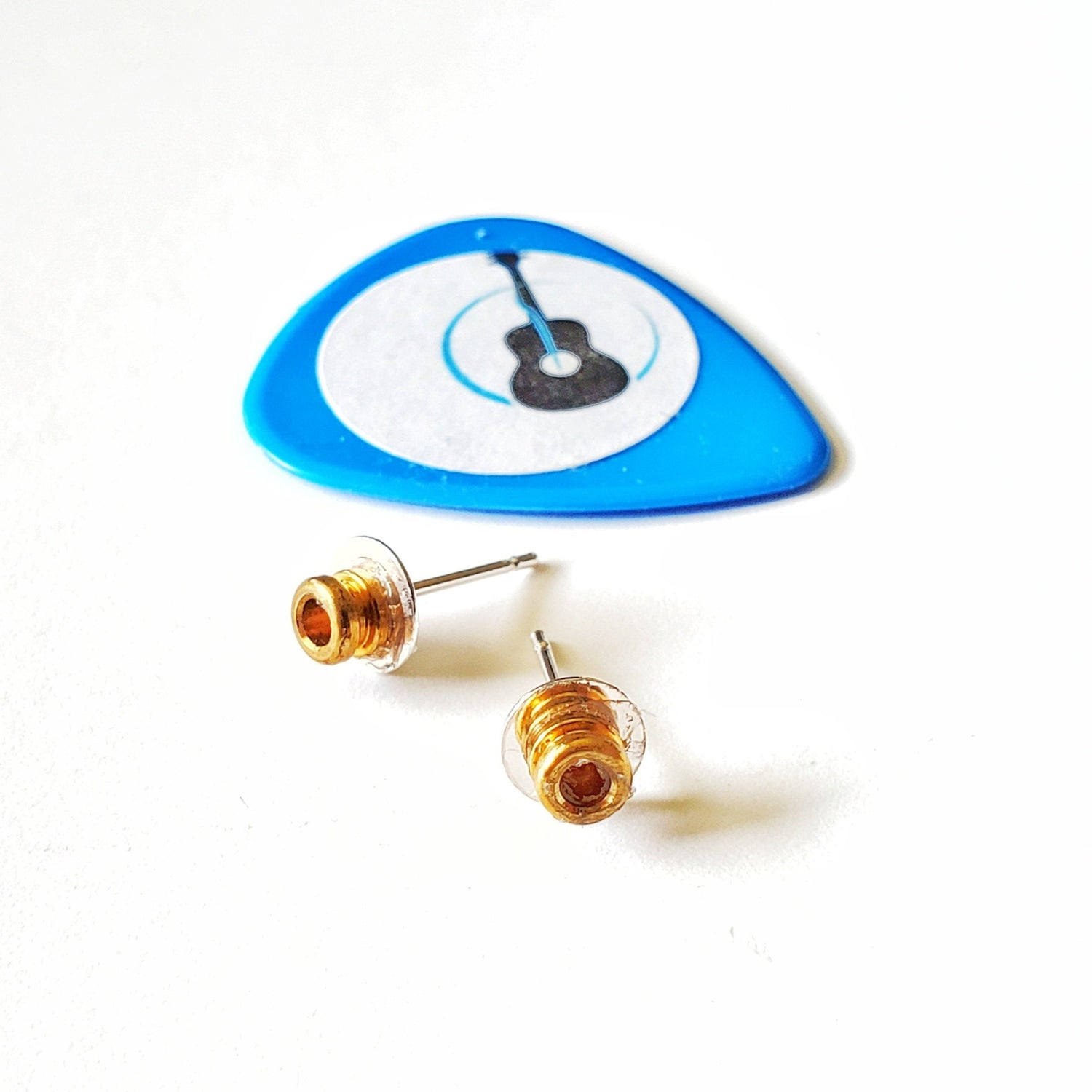 a pair of stud style earrings made from guitar string ballends above them is a blue guitar pick with a picture of a black guitar- white background