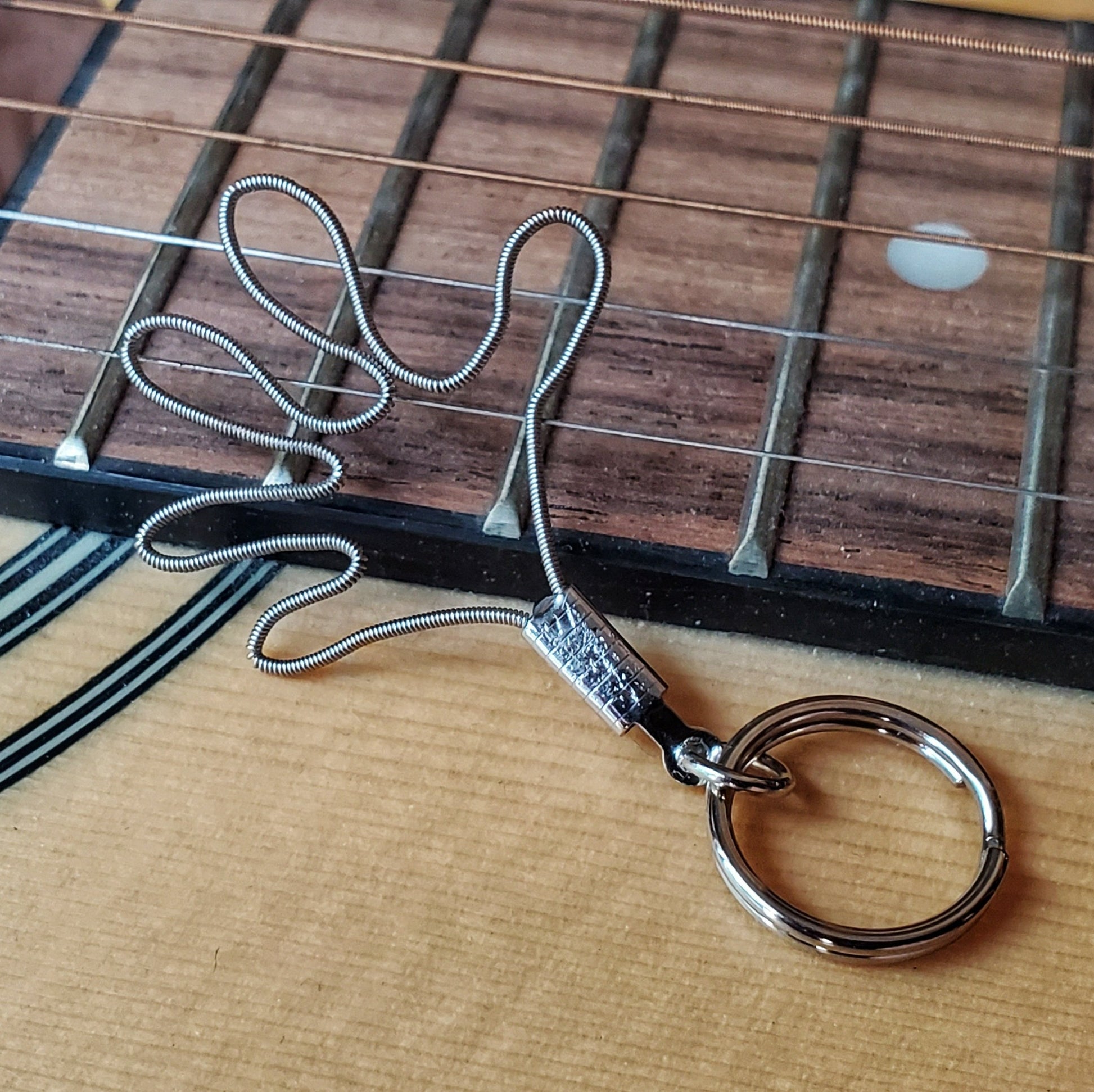 a keychain made from an upcycled guitar string shaped like a hand - behind it is the bridge of a beige guitar
