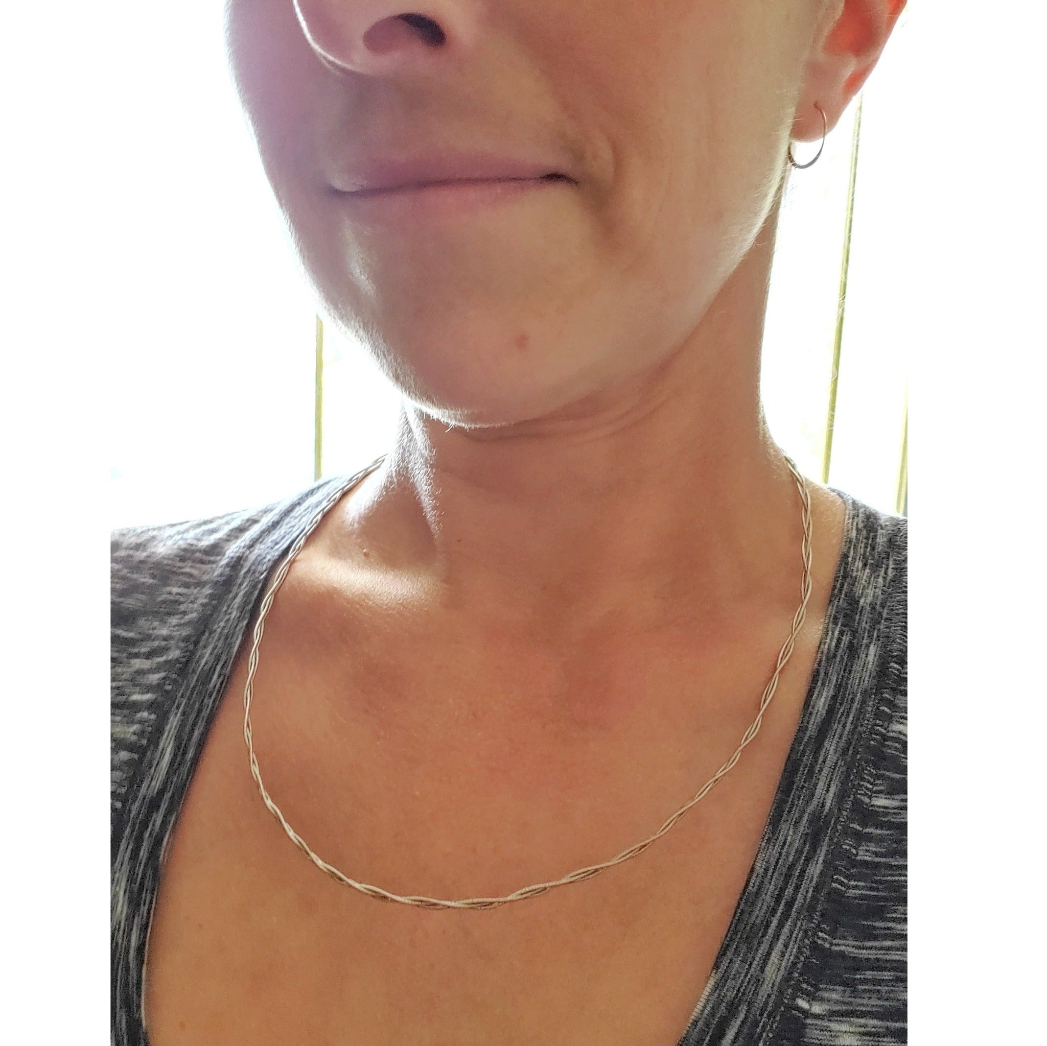 a woman's head and neck, she is wearing a silver chain made from braided guitar strings