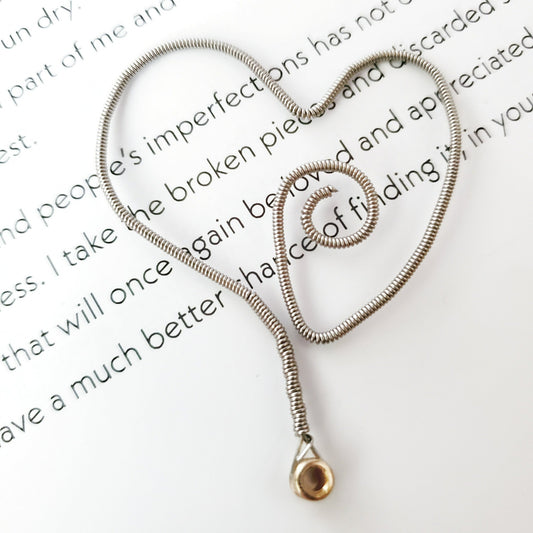 bookmark in the shape of a heart made from an upcycled guitar string - in the background are black words on a white background