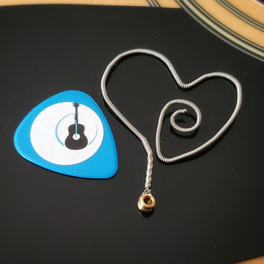 bookmark in the shape of a heart made from an upcycled guitar string - on the left is a blue guitar pick with an image of a black guitar- both are sitting on a black pick guard of a beige guitar