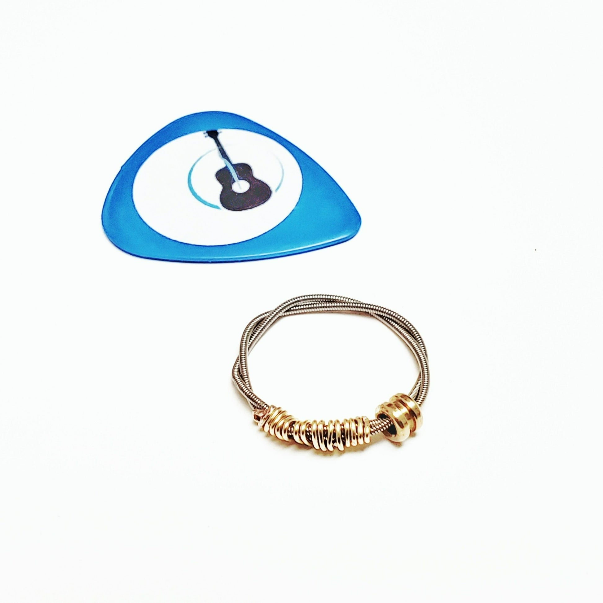 guitar string fidget ring with a gold coloured ballend above it is a blue guitar pick with an image of a black guitar - white background