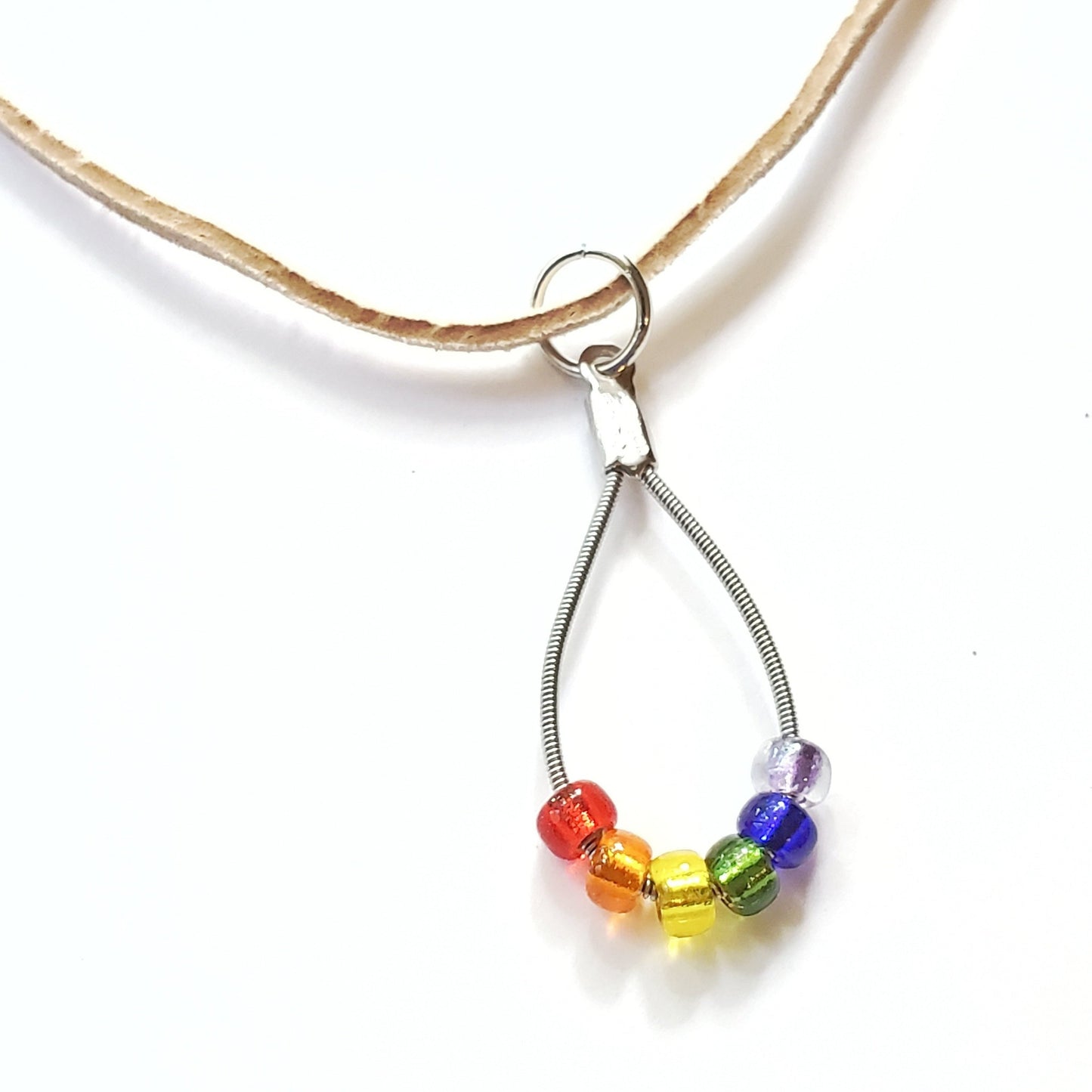 close-up of a necklace made from an upcycled guitar string - 6 glass beads represent the colours of the LGBTQ flag (red, orange, yellow, green, blue and purple) and a beige suede cord - white background