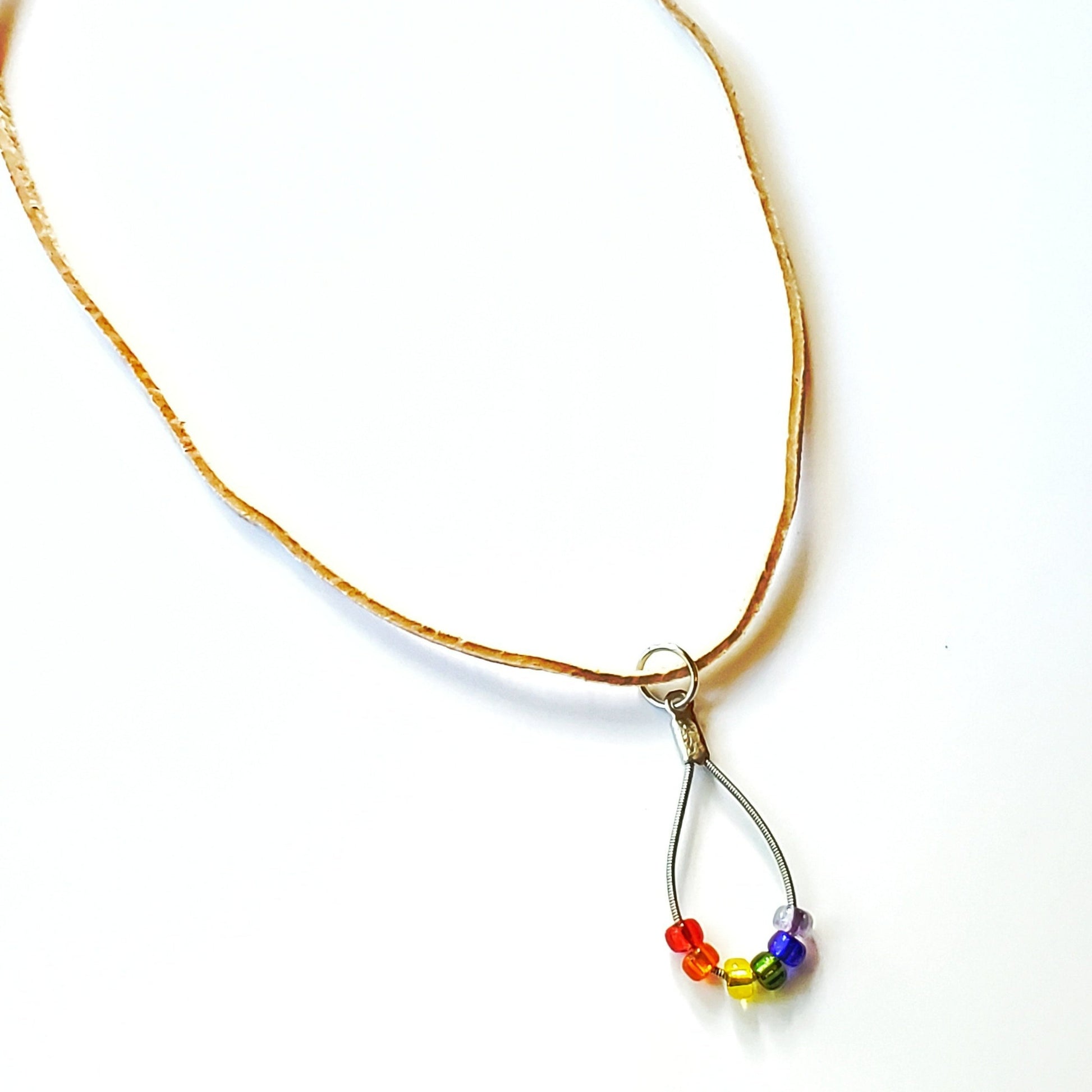 necklace made from an upcycled guitar string - 6 glass beads represent the colours of the LGBTQ flag (red, orange, yellow, green, blue and purple) and a beige suede cord - white background