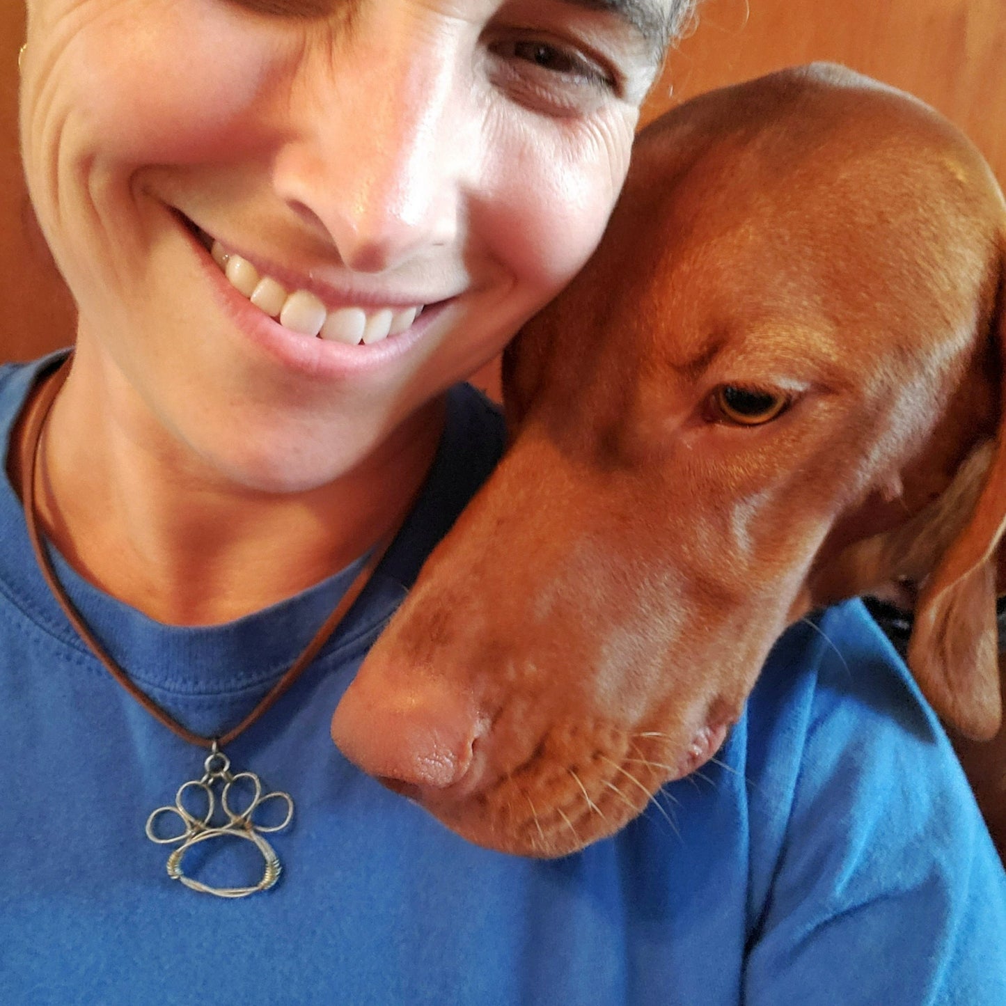 bottom of a woman's face wearing blue t-shirt and a necklace - necklace has a paw print pendant made from an upcycled guitar string - head of a vizsla