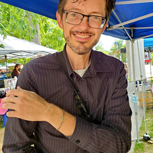 Man with glasses and a striped shirt wearing a silver coloured clasp style bracelet made from upcycled upright bass strings