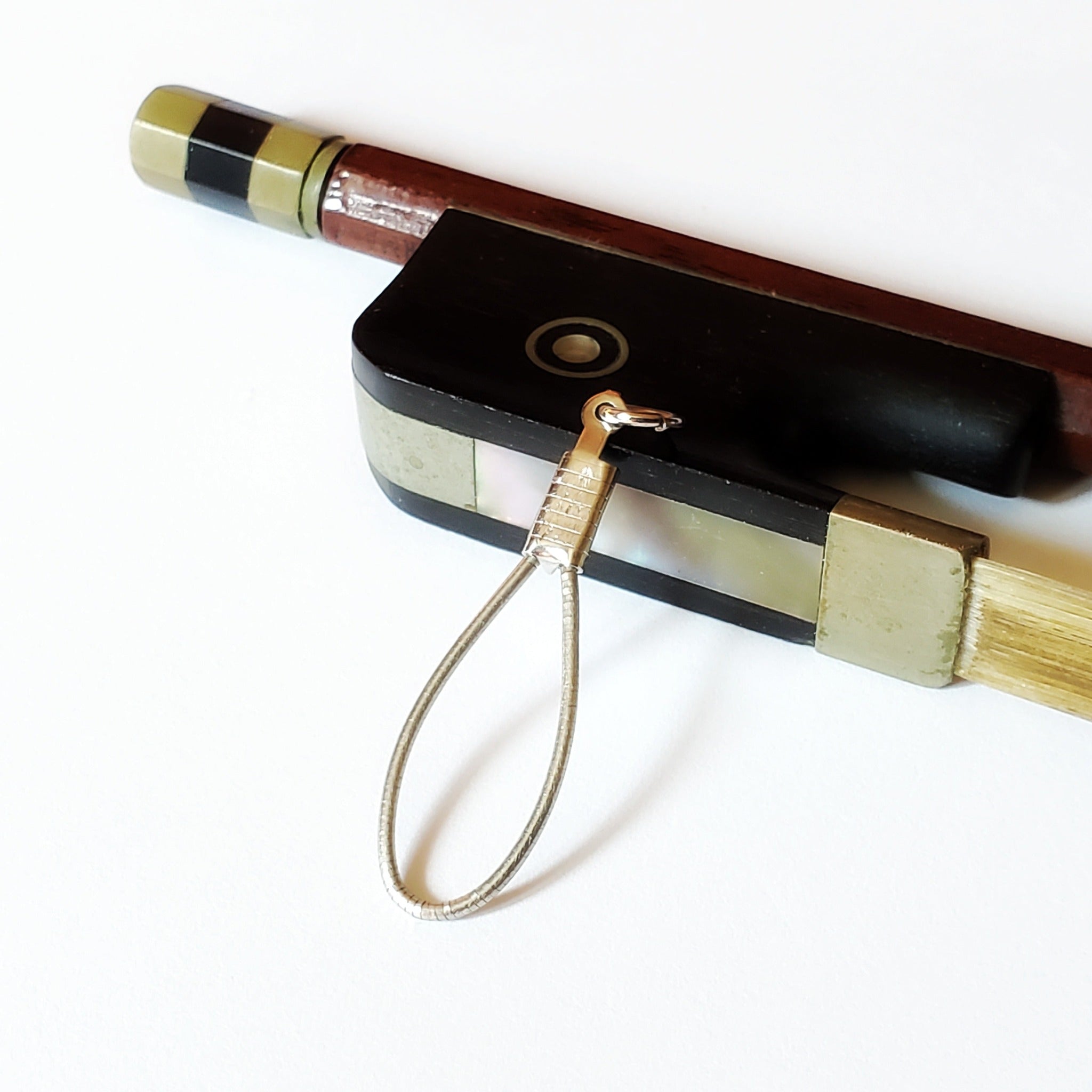 a silver coloured pendant made from an upcycled cello string - resting on a violin bow - white background