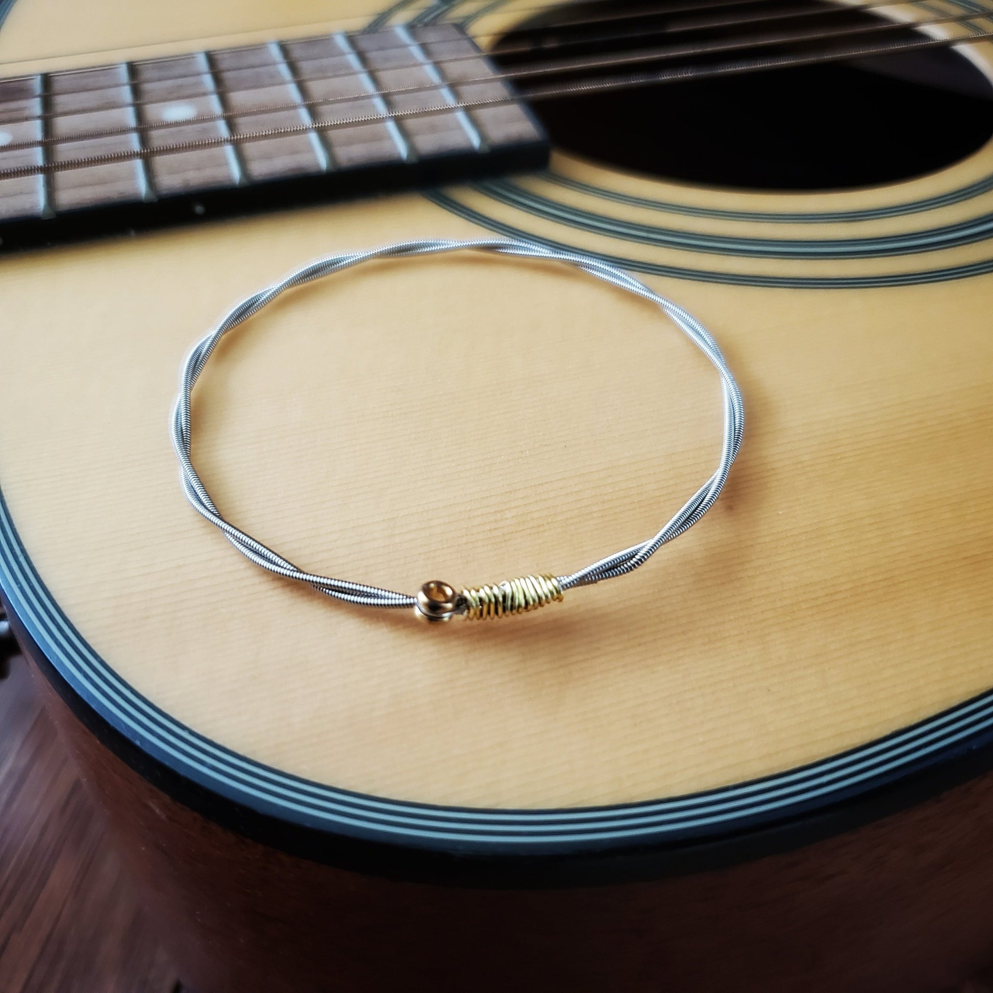 bangle style bracelet made from an upcycled guitar string is sitting on a tan coloured guitar