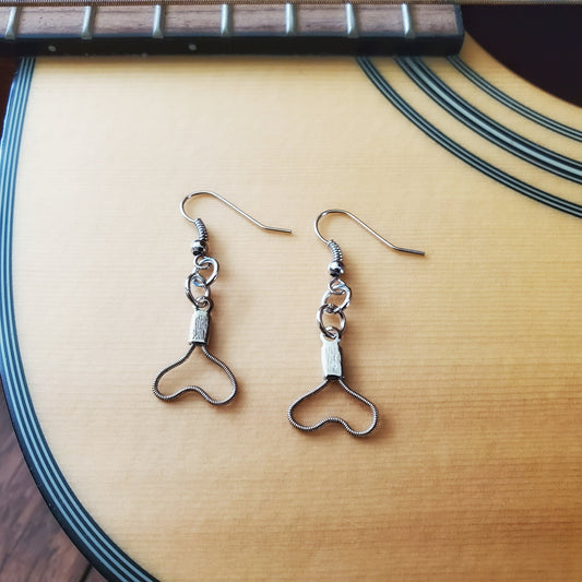 pair of earrings in the shape of upside down hearts, made from upcycled guitar strings - sitting on the body of a beige guitar