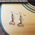 pair of earrings in the shape of upside down hearts, made from upcycled guitar strings - sitting on the body of a beige guitar