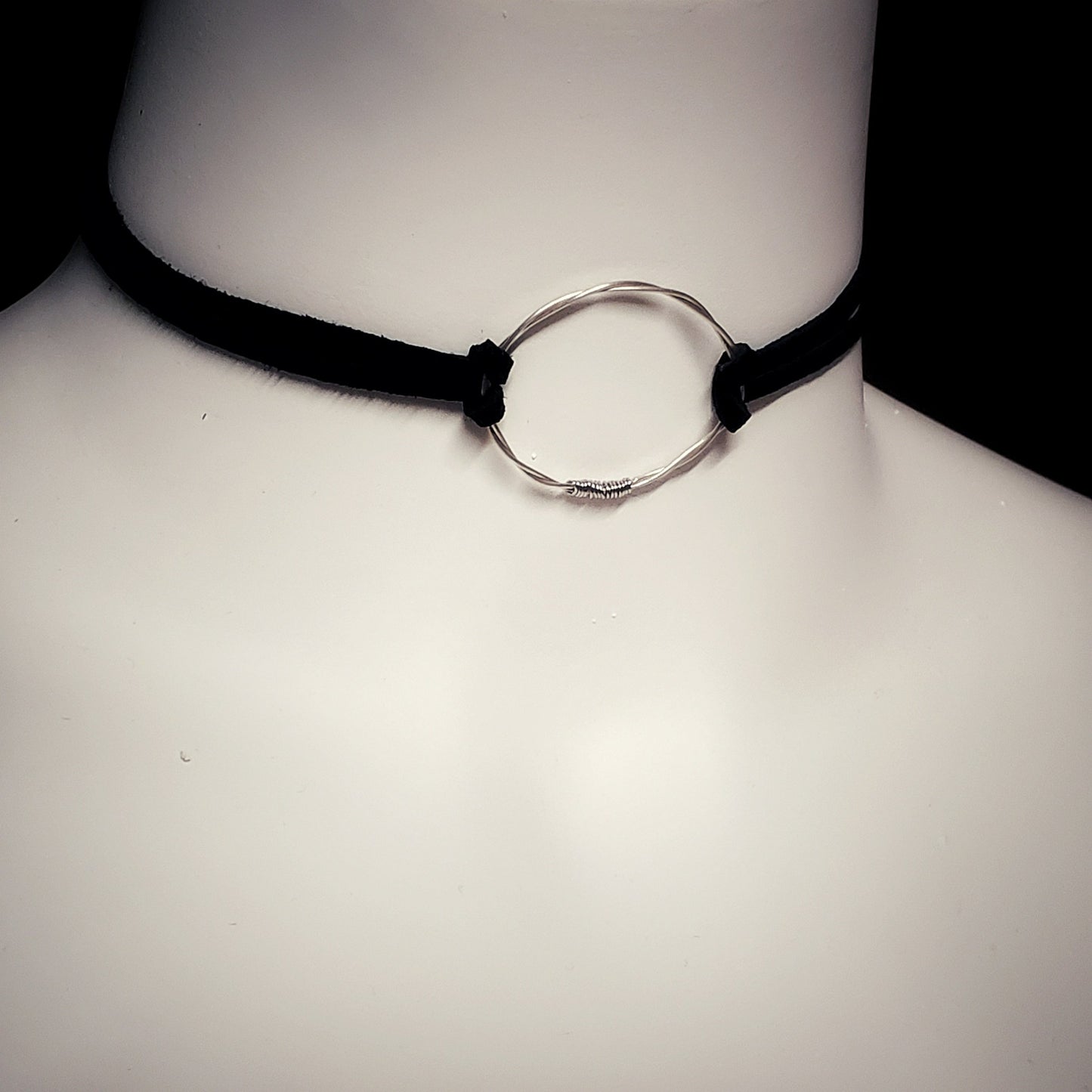 white bust - on the neck there is a choker style necklace - in the middle is a circle made from a piece of upcycled violin string on either side there are black suede cords 