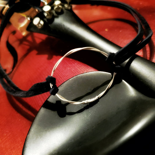 choker style necklace - in the middle is a circle made from a piece of upcycled violin string on either side there are black suede cords - the necklace sits on the chin rest of a violin