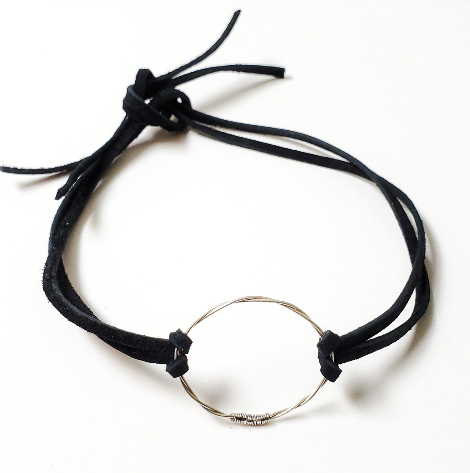 choker style necklace - in the middle is a circle made from a piece of upcycled violin string on either side there are black suede cords - white background