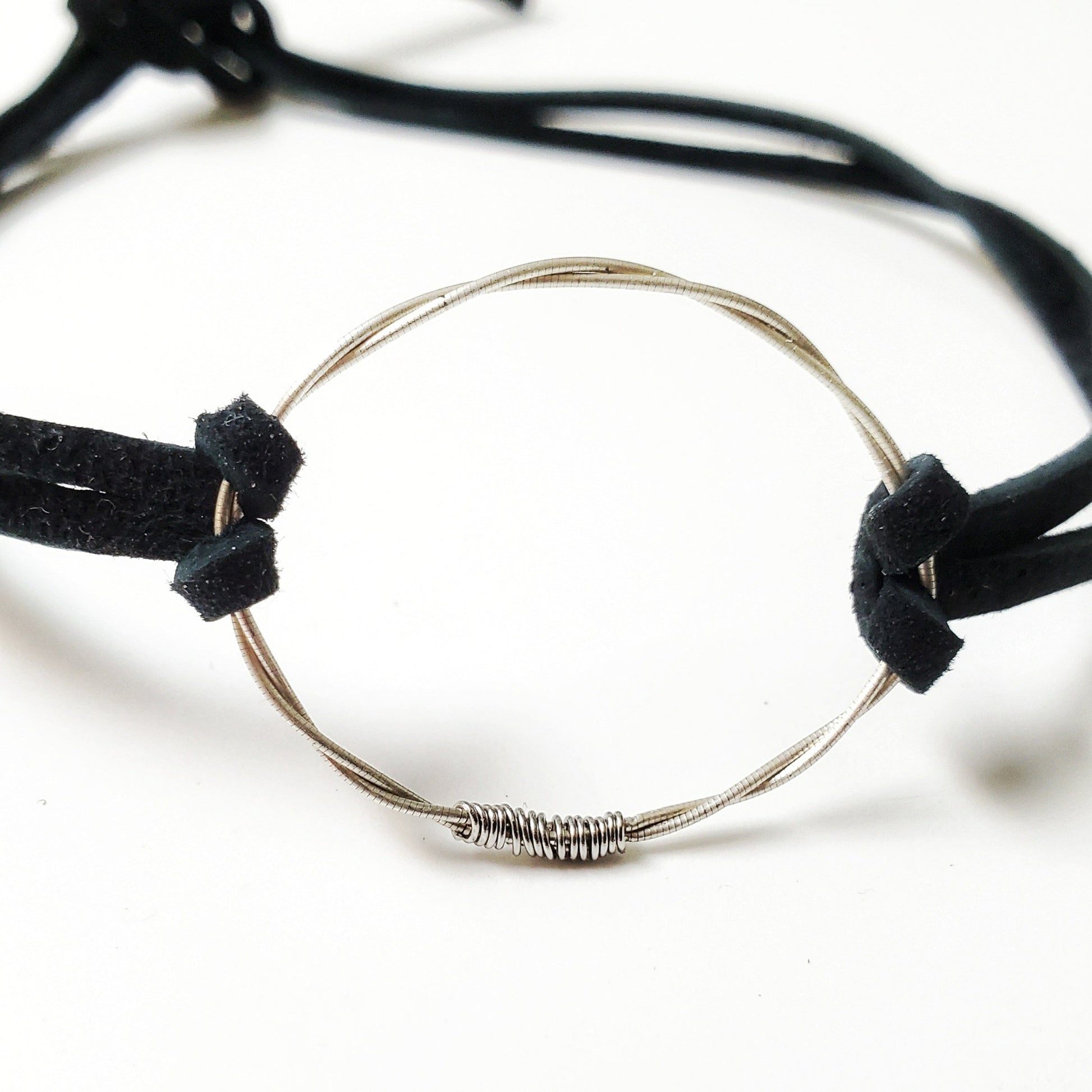 close-up of a choker style necklace - in the middle is a circle made from a piece of upcycled violin string on either side there are black suede cords 