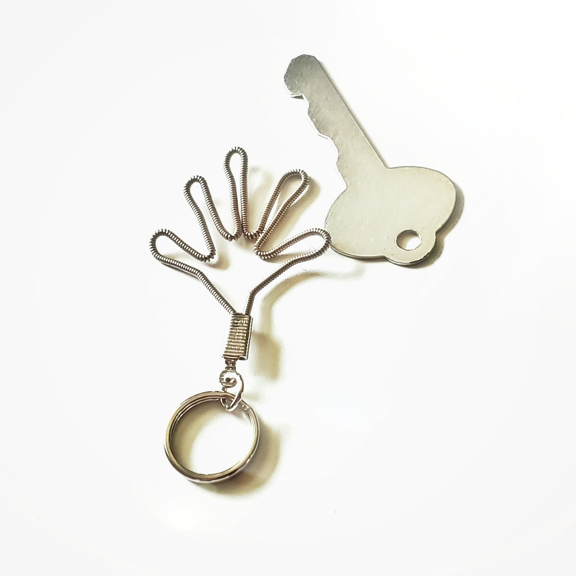 a keychain made from an upcycled guitar string shaped like a hand - beside it is a silver key- white background