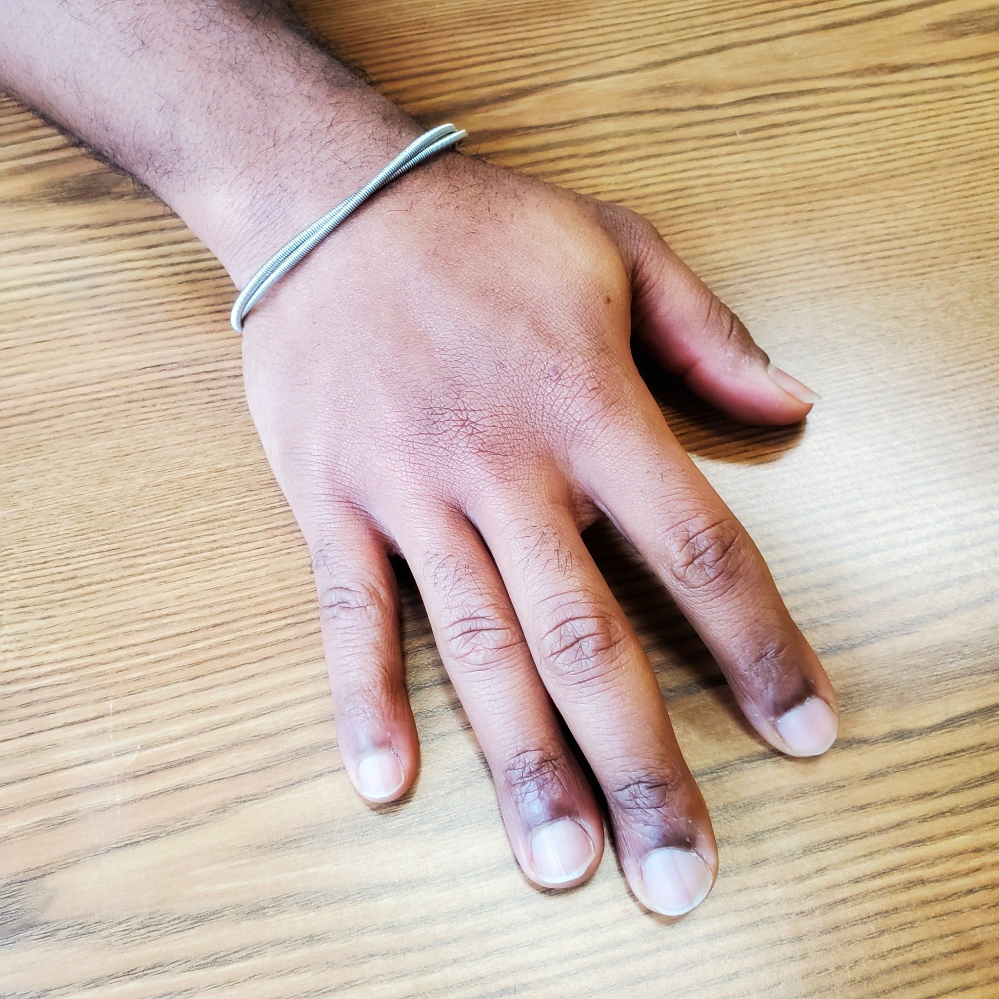 man's hand and wrist  on his wrist he is wearing a silver coloured bracelet made from 2 strands of upcycled electric bass strings