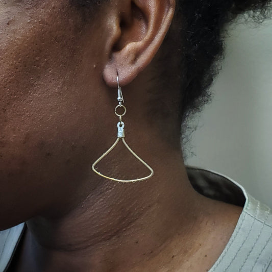 side of a woman's hanging on her ear is a gold coloured earring made from an upcycled guitar string in the shape of a triangle