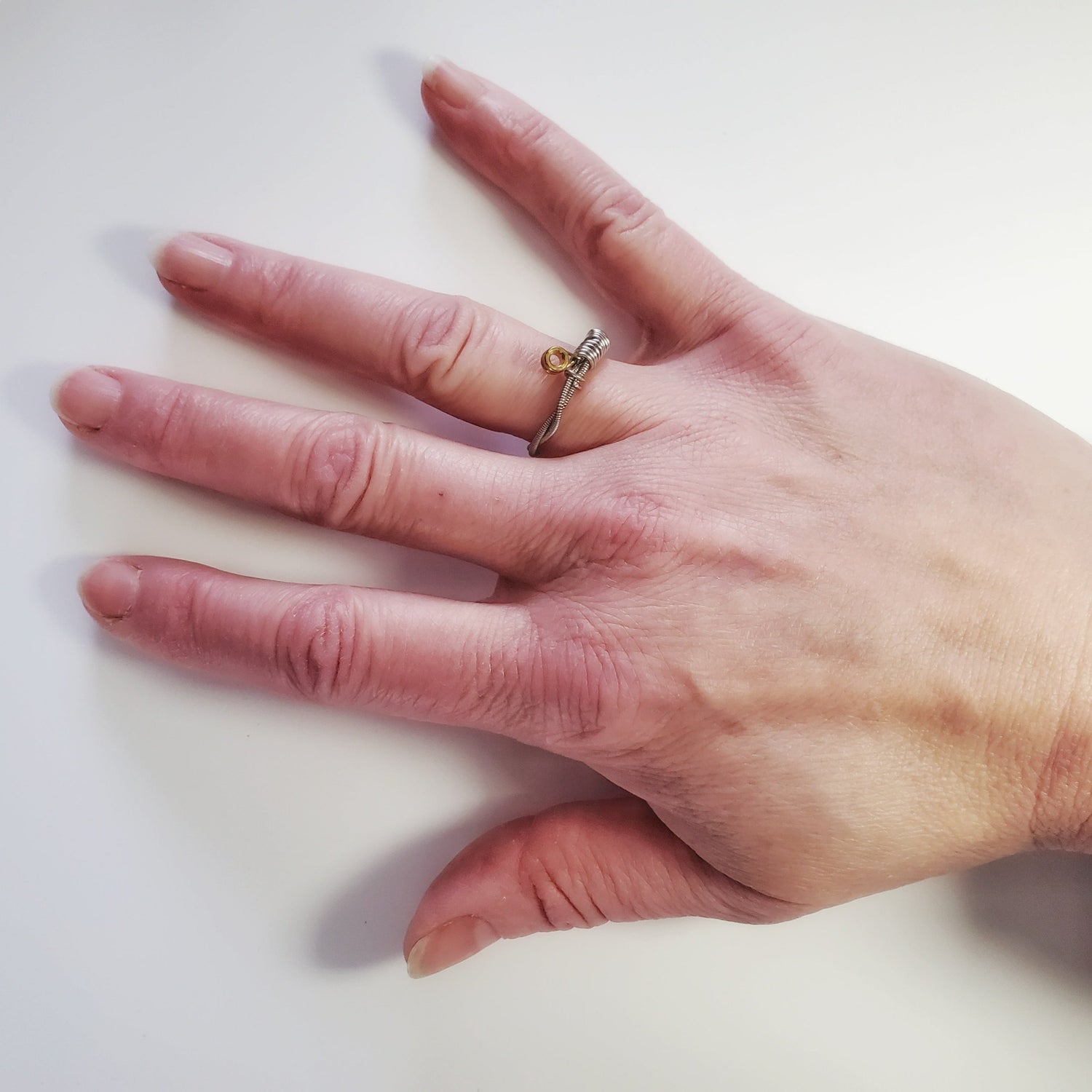 a woman's hand wearing a guitar string ring - white background