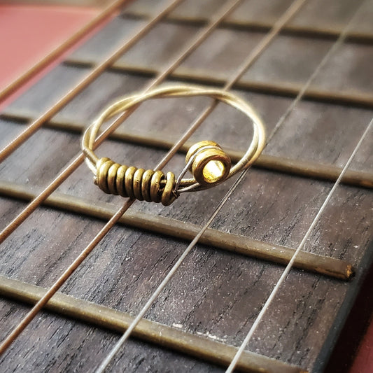 a gold coloured guitar string ring sitting on the neck of a guitar