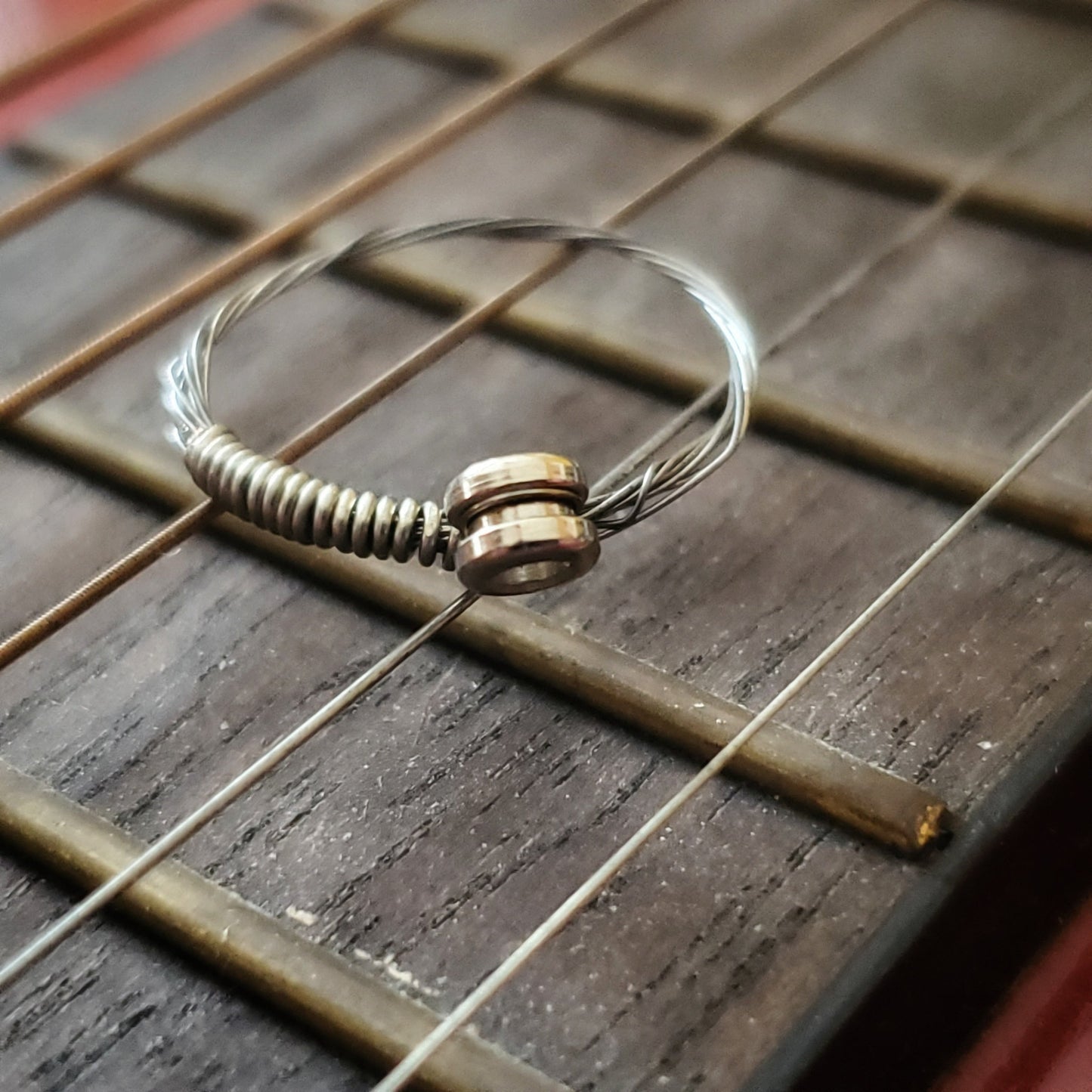 Simple Silver Guitar String Ring with Ballend sitting on the neck of a guitar
