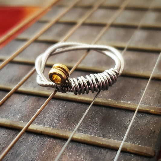 a silver coloured guitar string ring is sitting on the neck of a guitar