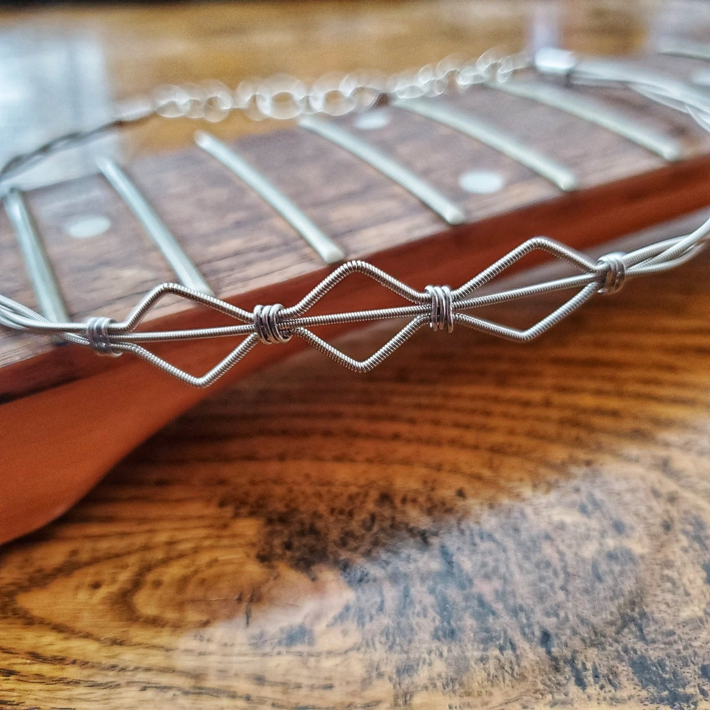  a necklace in the shape of 3 diamonds made from - sits on the neck of a guitar which has no strings
