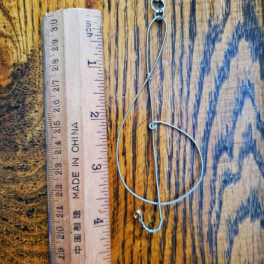 rearview mirror decoration in the shape of a treble clef, made from an upcycled guitar string- on the left is a beige ruler