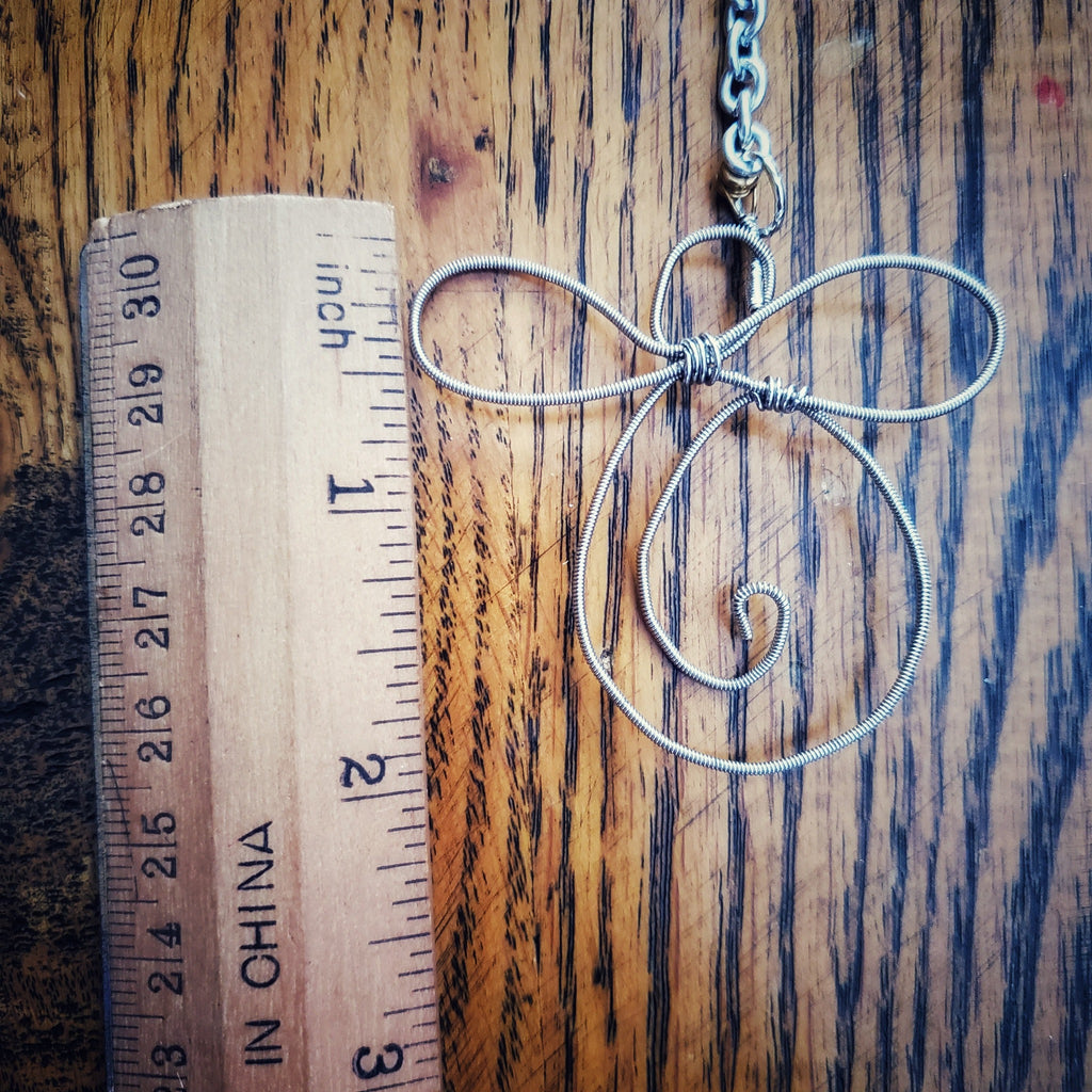 rearview mirror decoration shaped like an angel made from an upcycled guitar string on the left is a beige ruler