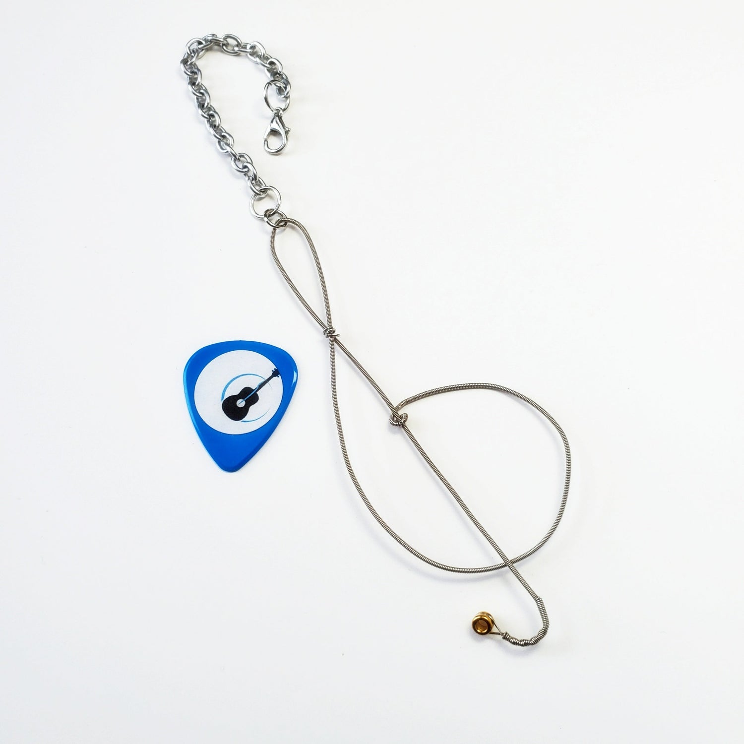 rearview mirror decoration in the shape of a treble clef, made from an upcycled guitar string- beside it is a blue guitar pick with an image of a black guitar