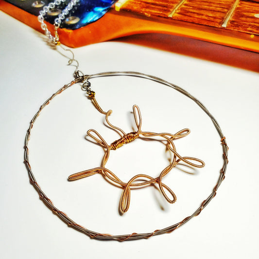 a decoration shaped like a sun with a circle around it hanging off a chain - the sun and circle are made from upcycled guitar strings - above there is a guitar neck with no strings - white background