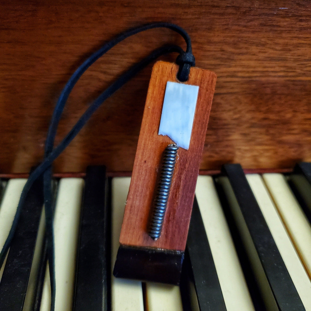 a necklace the pendant of which is made from upcycled pieces of wood, string, ebony and ivory from a piano as well as a leather cord - the necklace sits on some piano keys