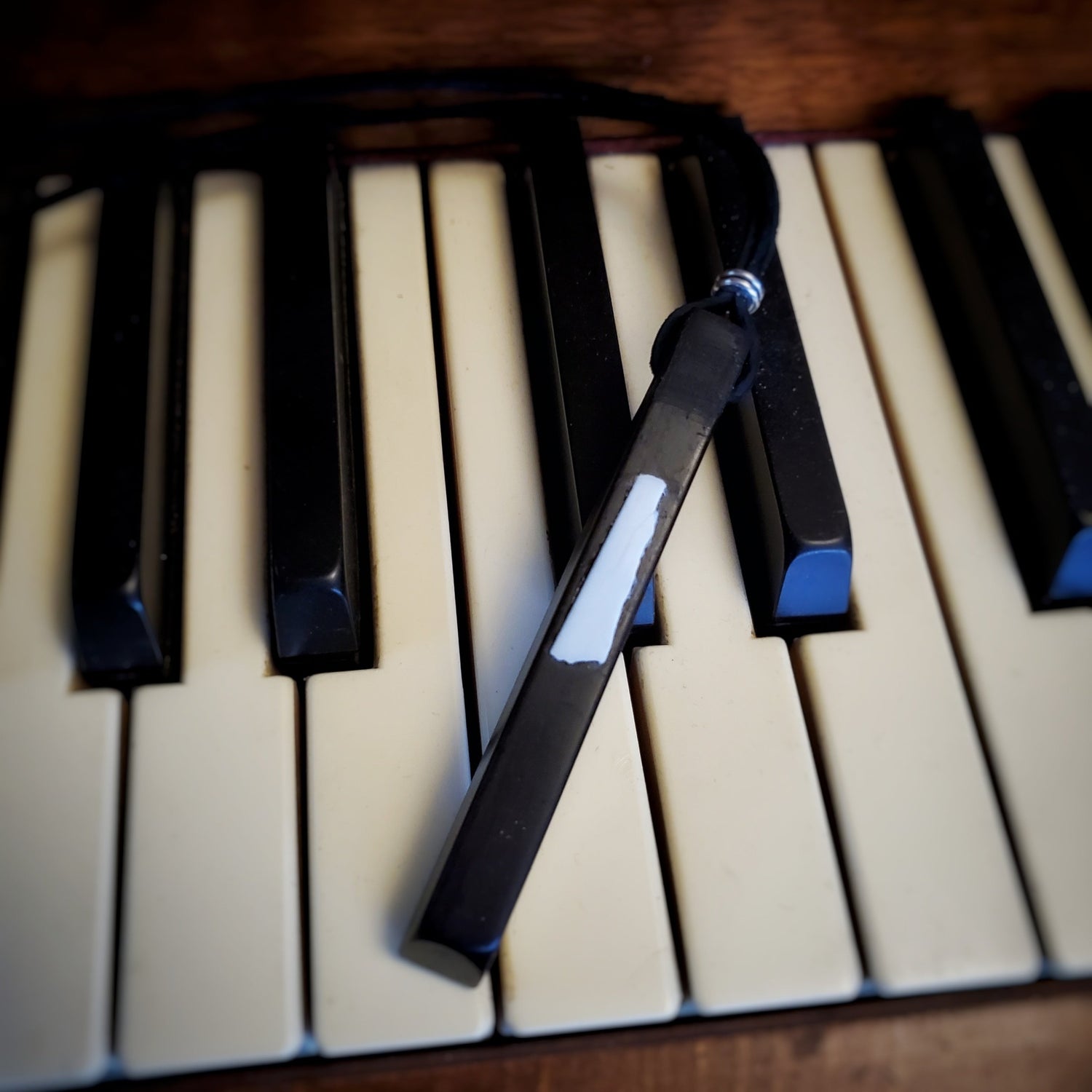 necklace made from an ebony piano key and a piece of piano key ivory with a leather lanyard sitting on a set of piano keys
