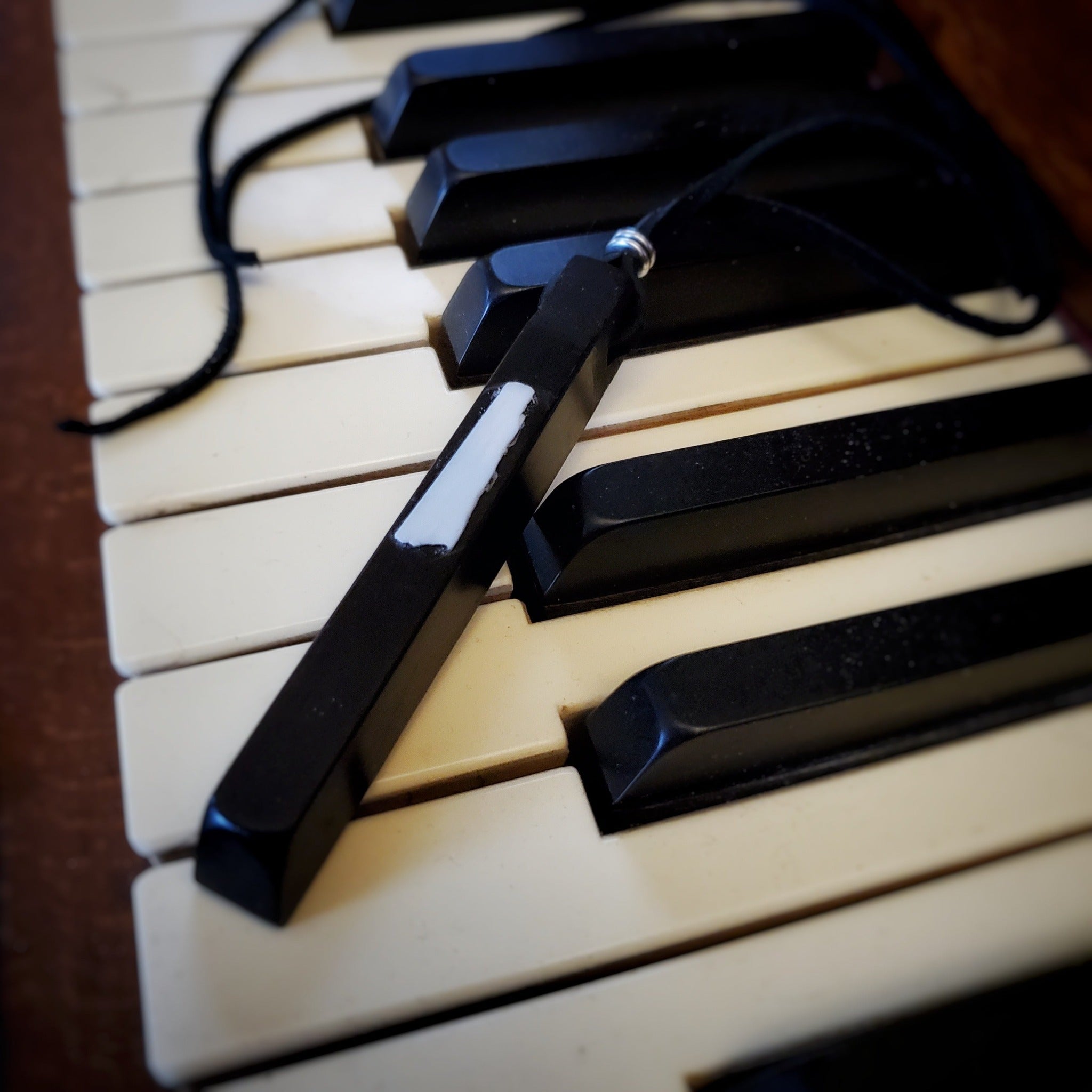 necklace made from an ebony piano key and a piece of piano key ivory with a leather lanyard sitting on a set of piano keys