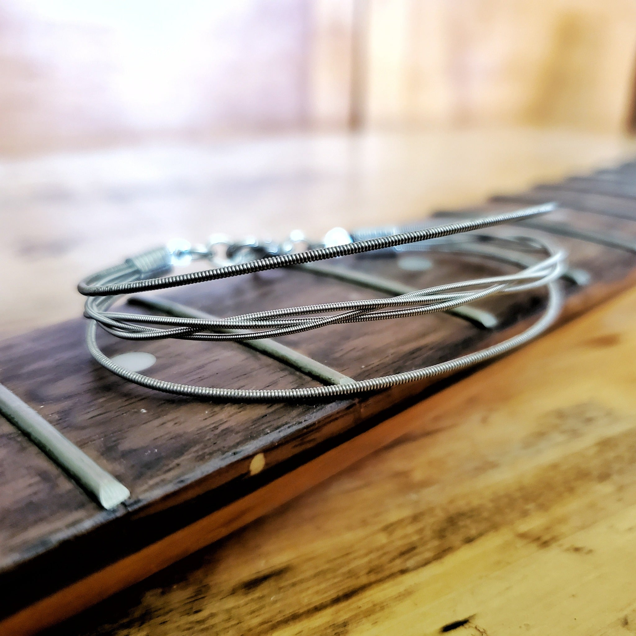 a silver coloured bracelet - between 2 guitar strings, 3 others are braided - the bracelet rests on the neck of a guitar