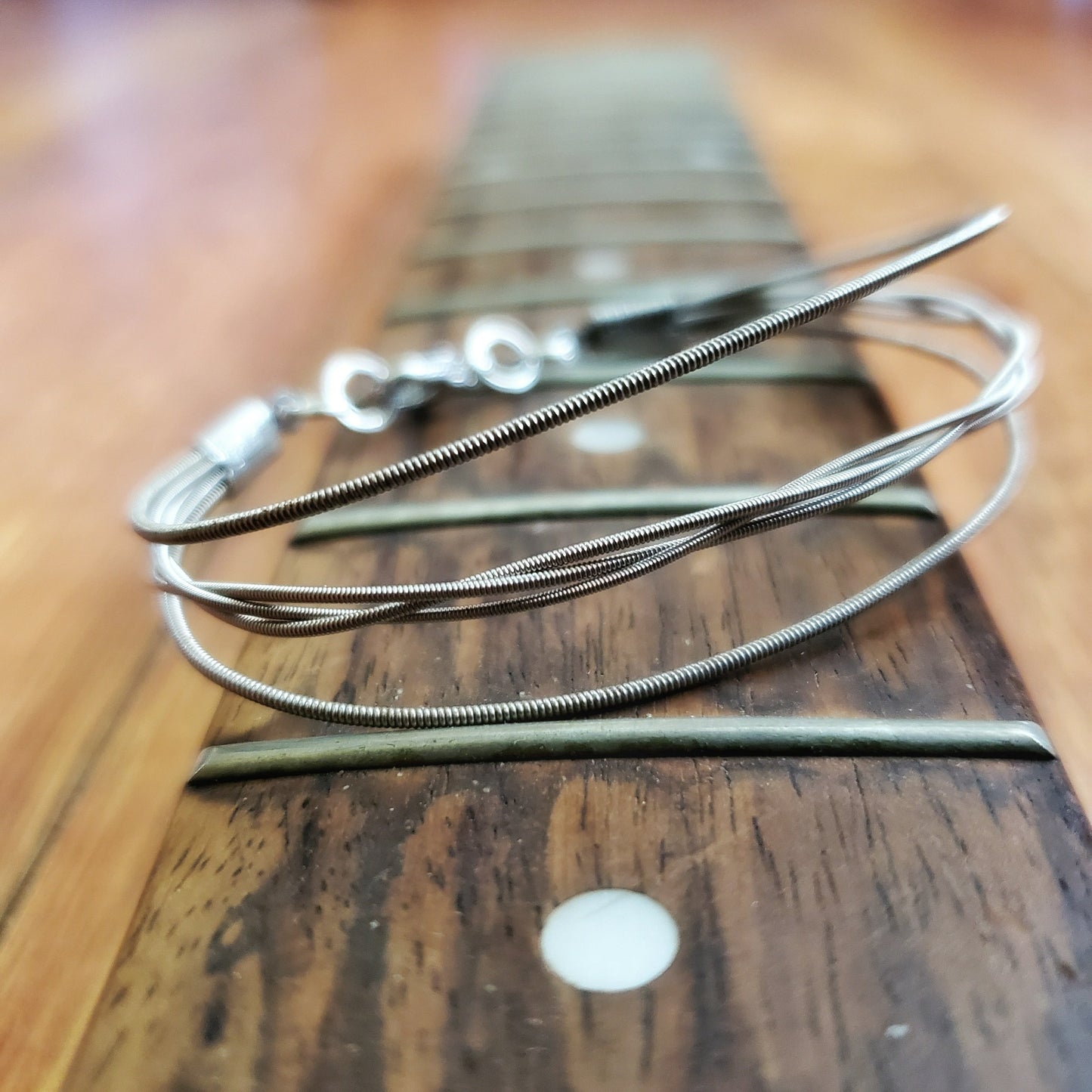 a silver coloured bracelet - between 2 guitar strings, 3 others are braided - the bracelet rests on the neck of a guitar which doesn't have any strings