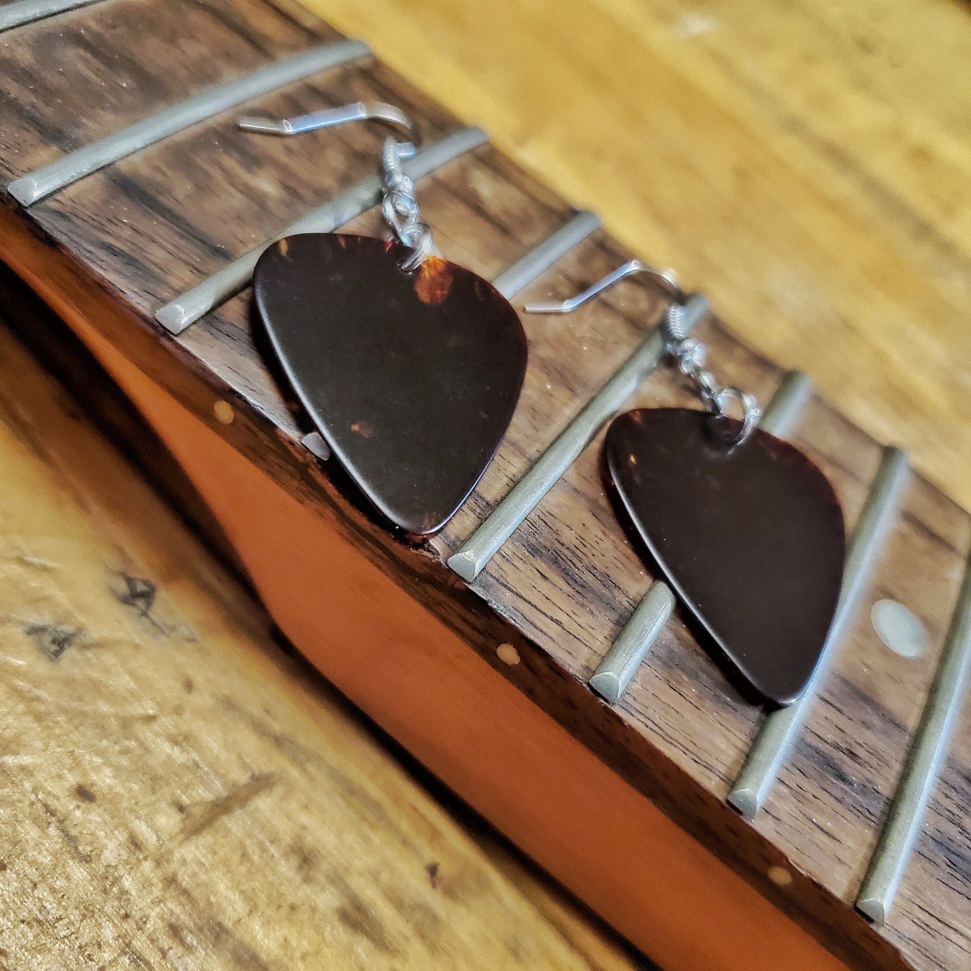 earrings made from turtle shell brown guitar picks sitting on the neck of a guitar from which the strings have been removed
