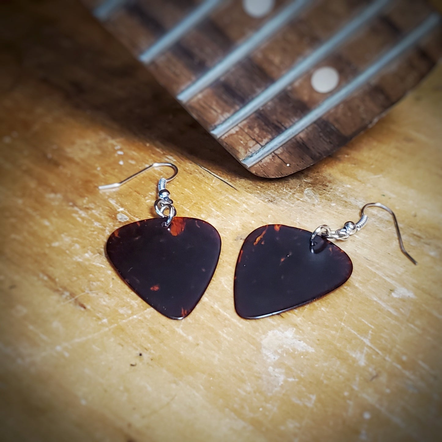 earrings made from turtle shell brown guitar picks sitting under he neck of a guitar from which the strings have been removed