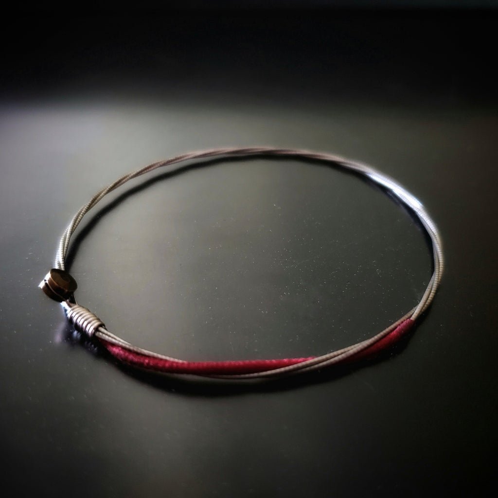 a red and silver coloured bracelet made from an upcycled cello string bracelet on a black background
