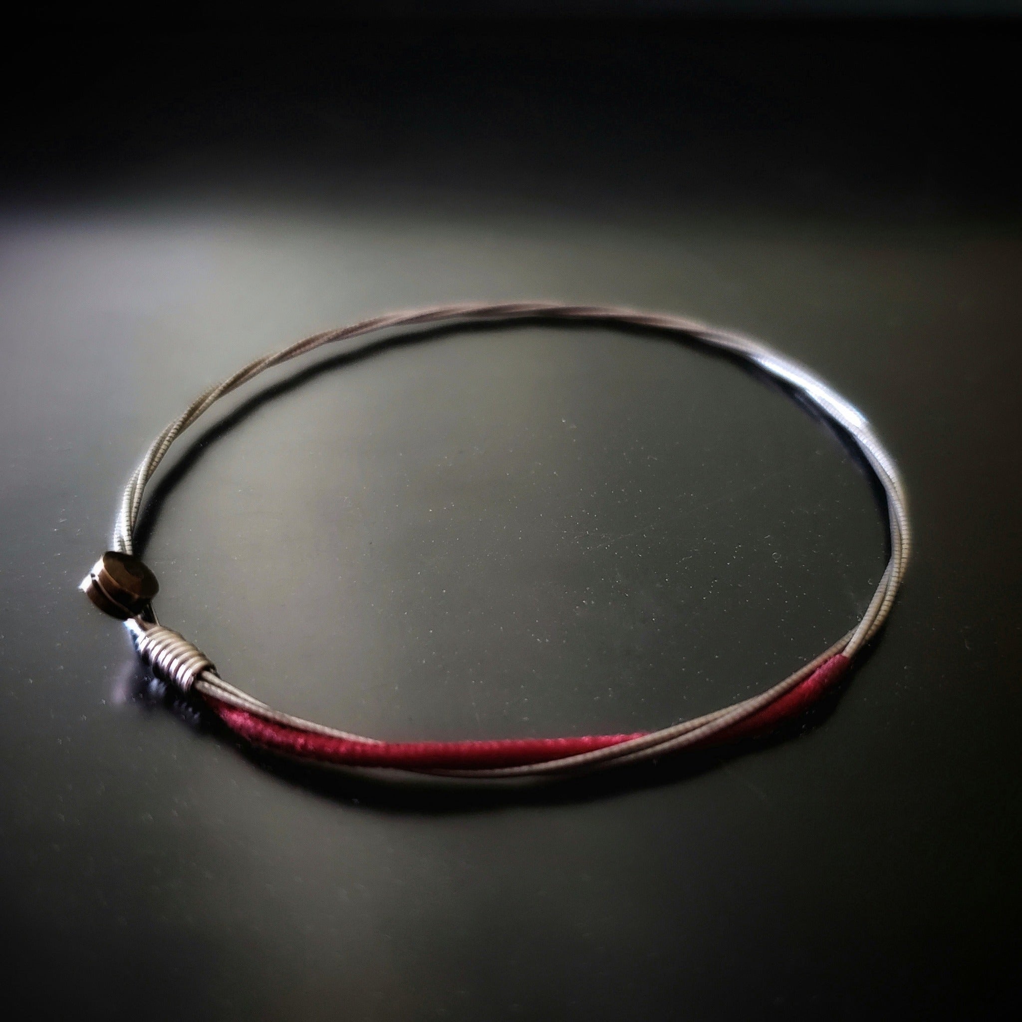 a red and silver coloured bracelet made from an upcycled cello string bracelet on a black background