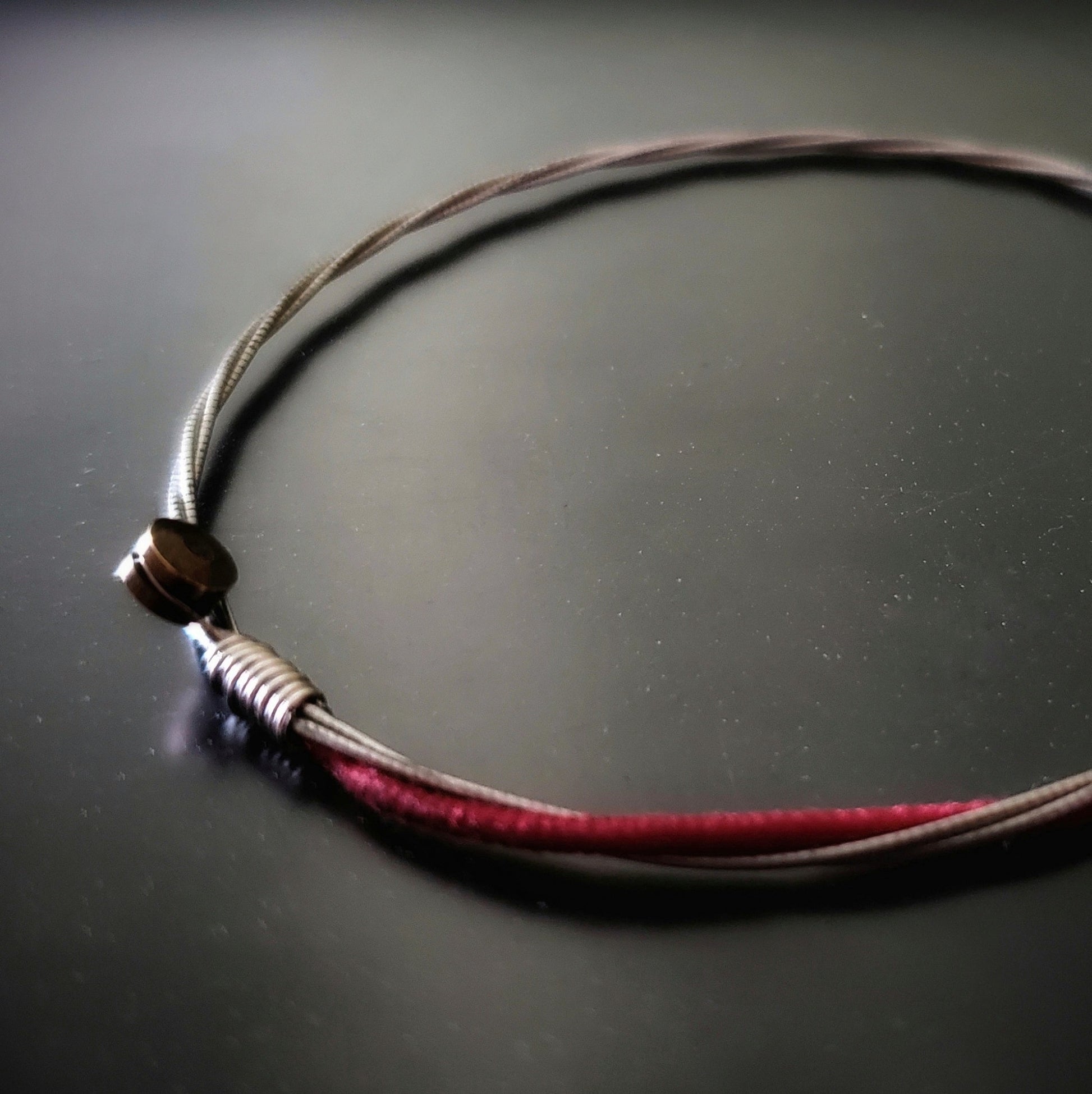 a red and silver coloured bracelet made from an upcycled cello string bracelet on a black background