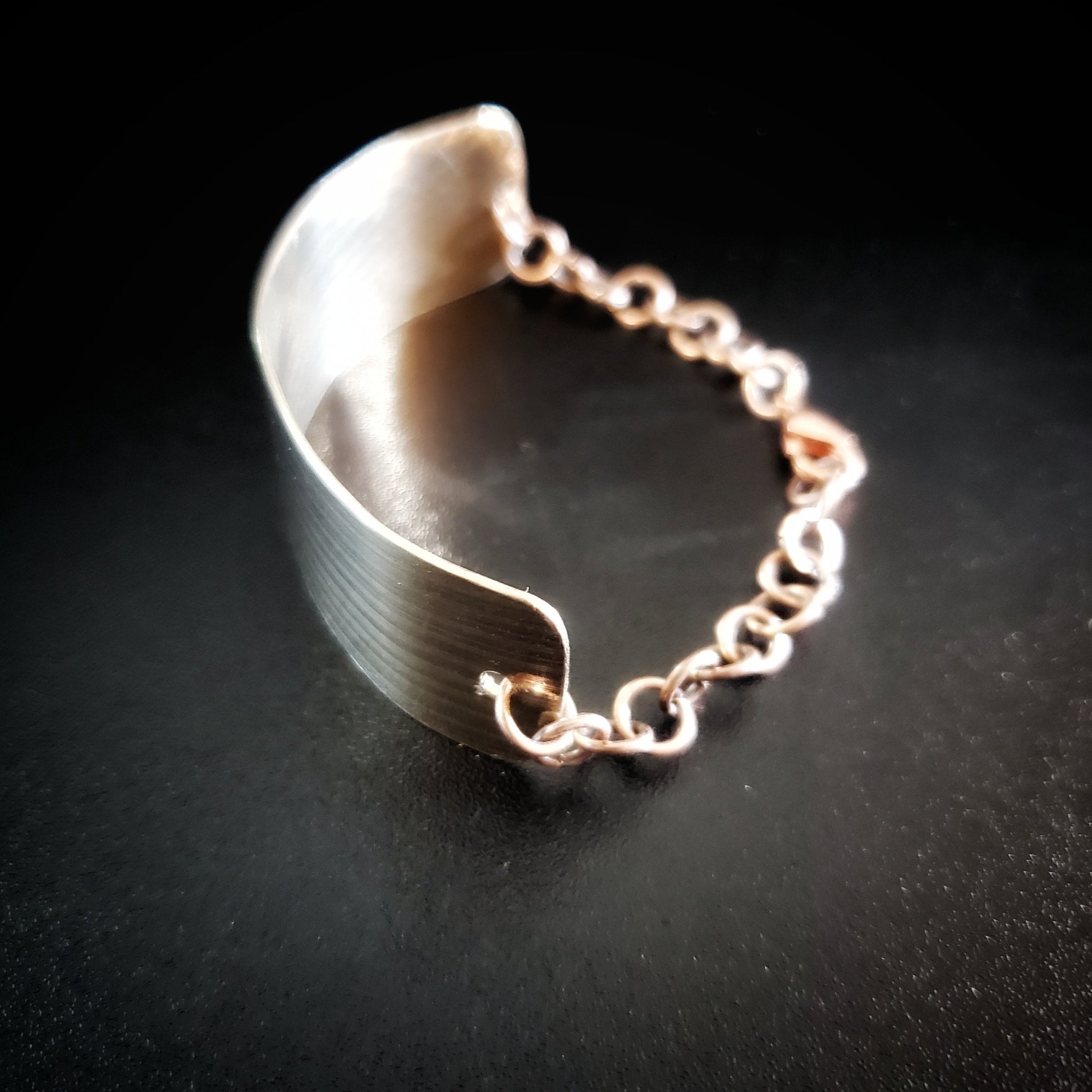 bracelet made from a rectangular piece of upcycled cymbal and copper coloured chain - black background