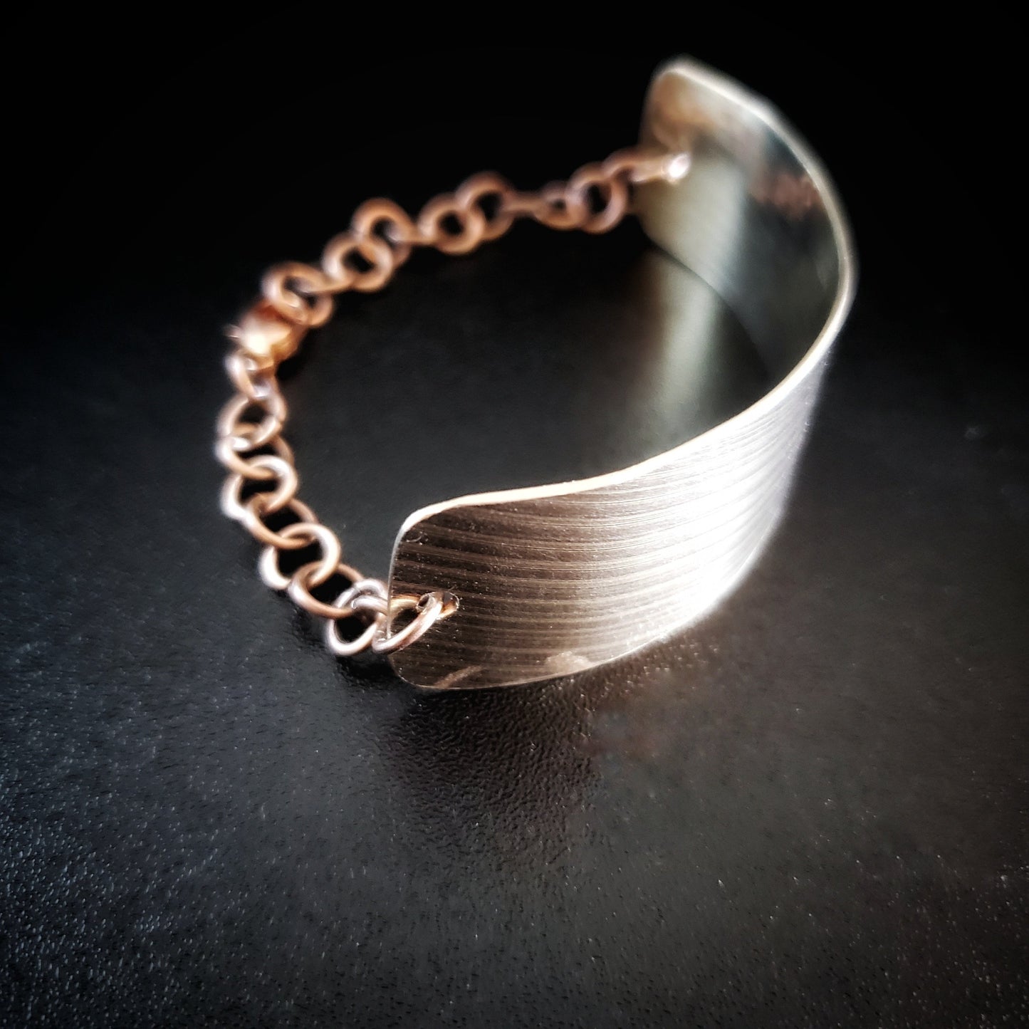 bracelet made from a rectangular piece of upcycled cymbal and copper coloured chain - black background