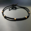 black bracelet made from a suede cord and gold coloured guitar string ballends